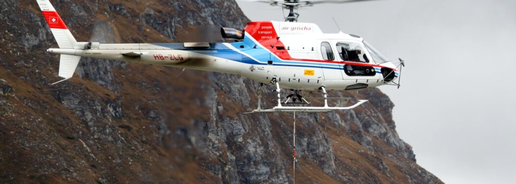 white and red helicopter flying near mountain terrain during daytime