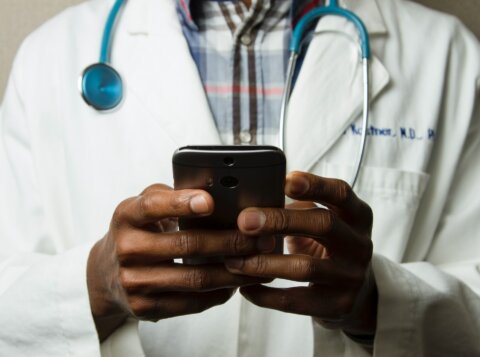 person wearing lavatory gown with green stethoscope on neck using phone while standing