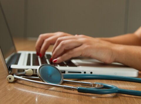 person sitting while using laptop computer and green stethoscope near