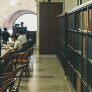 selective focus photography of books on bookcases near people sits in chairs