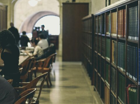 selective focus photography of books on bookcases near people sits in chairs