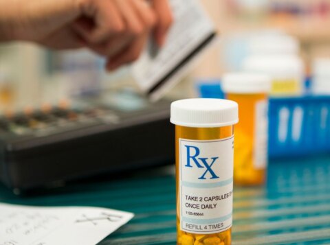 A prescription container pictured in front of someone's hand swiping a credit card