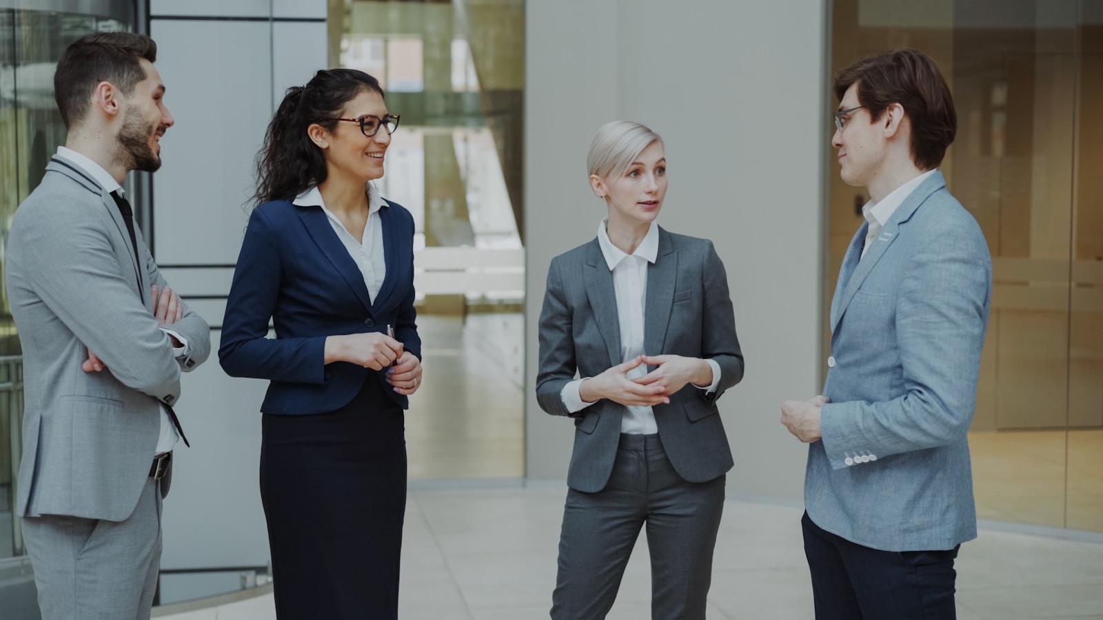 Four business professionals conversing in a modern office lobby.