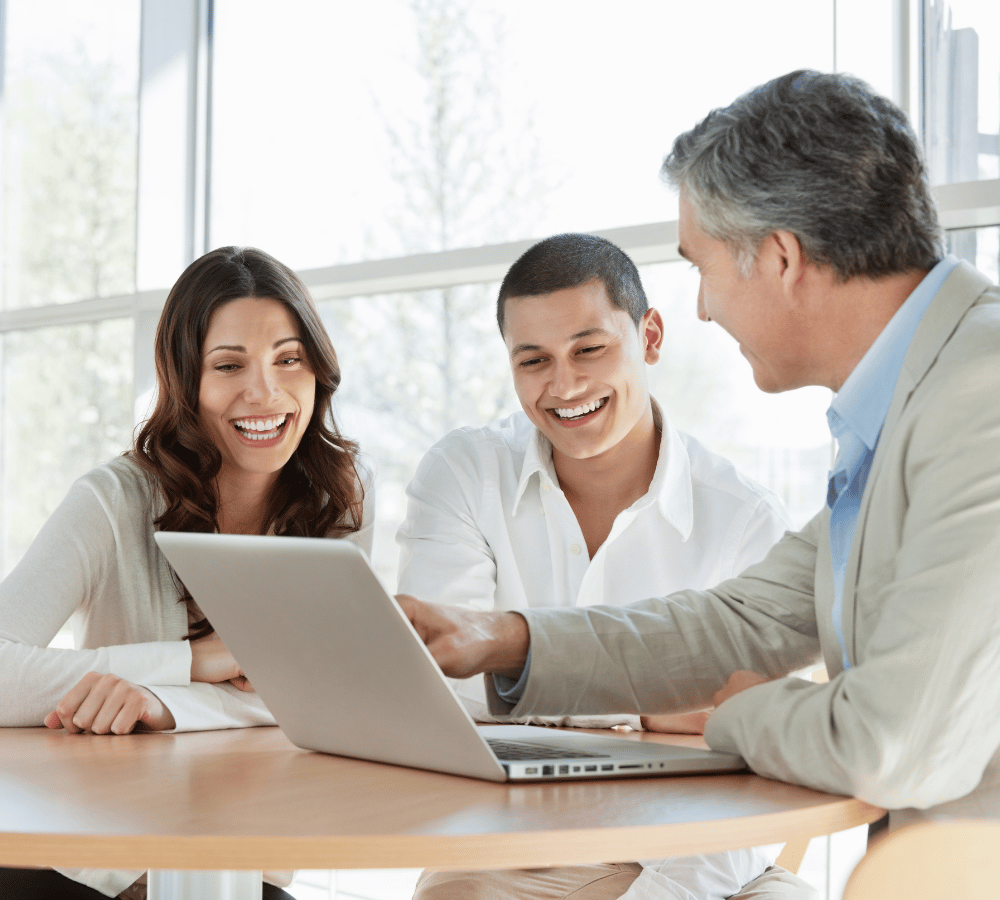 A man pointing to a computer screen with a man and woman smiling and looking at what he is pointing at
